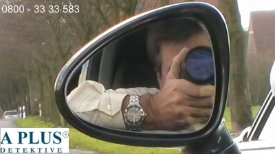 Detektiv Foto Detektiv sitzt im Fahrzeug und macht ein Foto einer Handlung. Die Abbildung zeigt den Detektiv im Seitenspiegel.